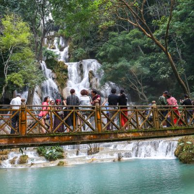 Luang Prabang, Laos - December 9, 2018: Male tourist on top of beautiful Tat Kuang Si(Xi) Waterfalls. It is one of the most popular tourist attractions in Laos. These waterfalls are a favorite side trip for tourists in Luang Prabang.